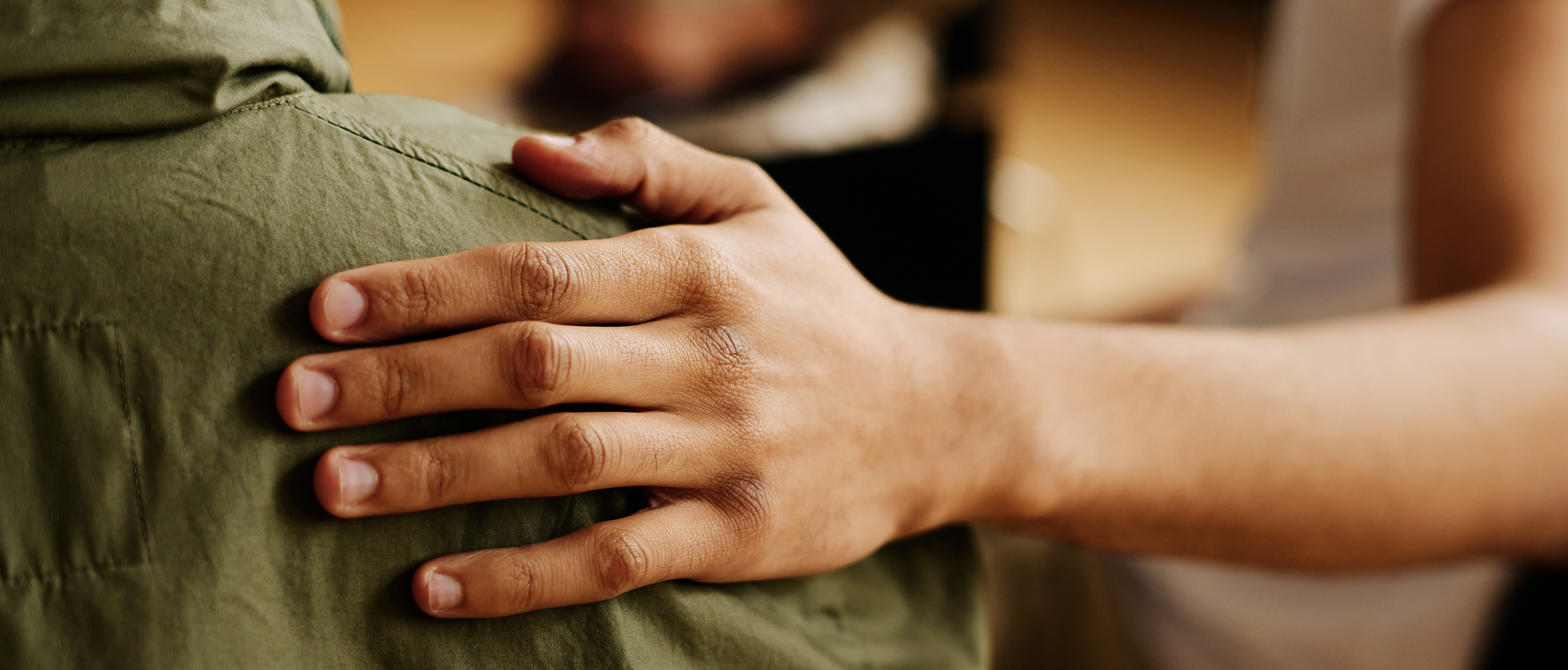 A person giving comfort to someone by placing their hand on their back
