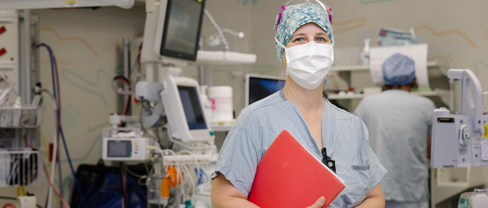 Nurse in operating room with mask, cap and clipboard.