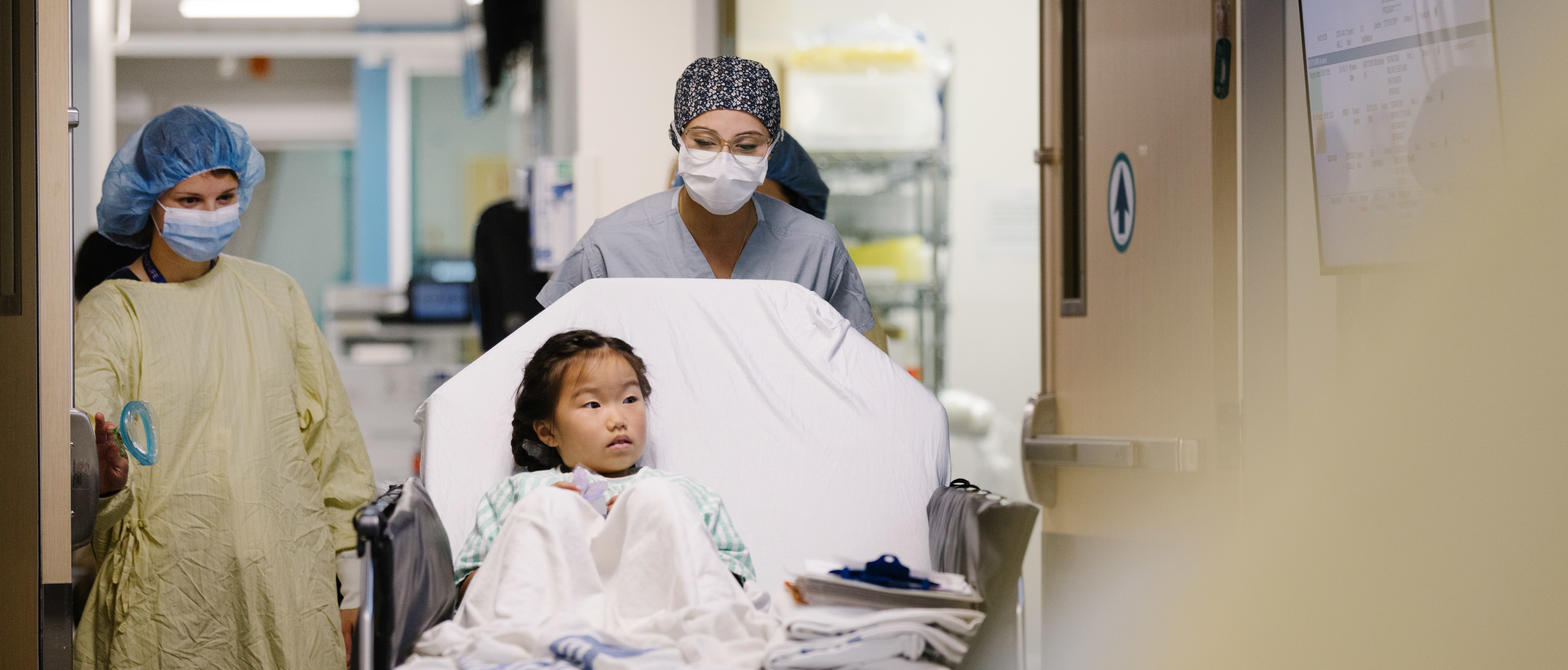 Child in gown being wheeled on bed by two surgical team members