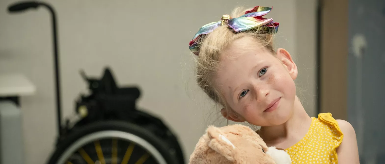 Smiling girl holding teddy with wheelchair in background