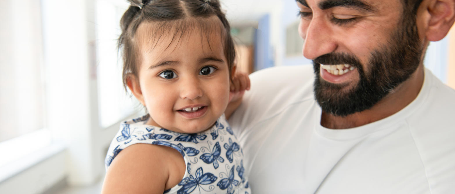A parent smiling while holding their child in a hallway