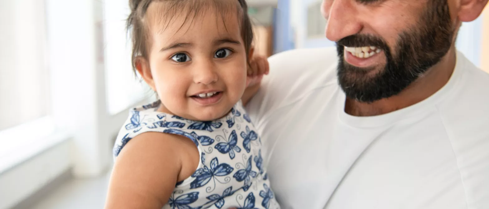 A parent smiling while holding their child in a hallway
