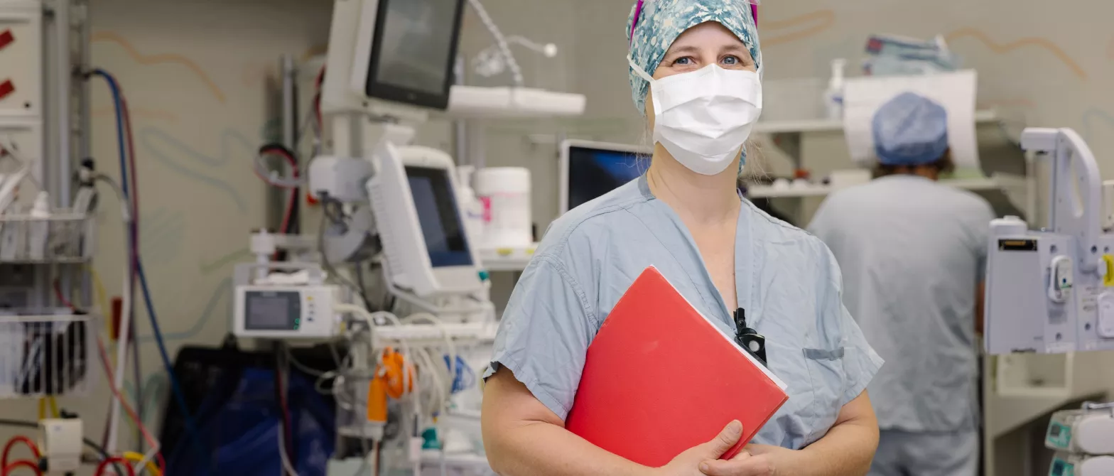 Nurse in operating room with mask, cap and clipboard.