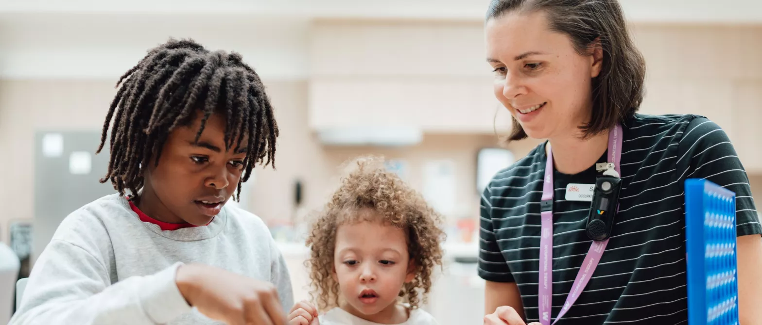 Occupational Therapist working with two children to put a puzzle together.