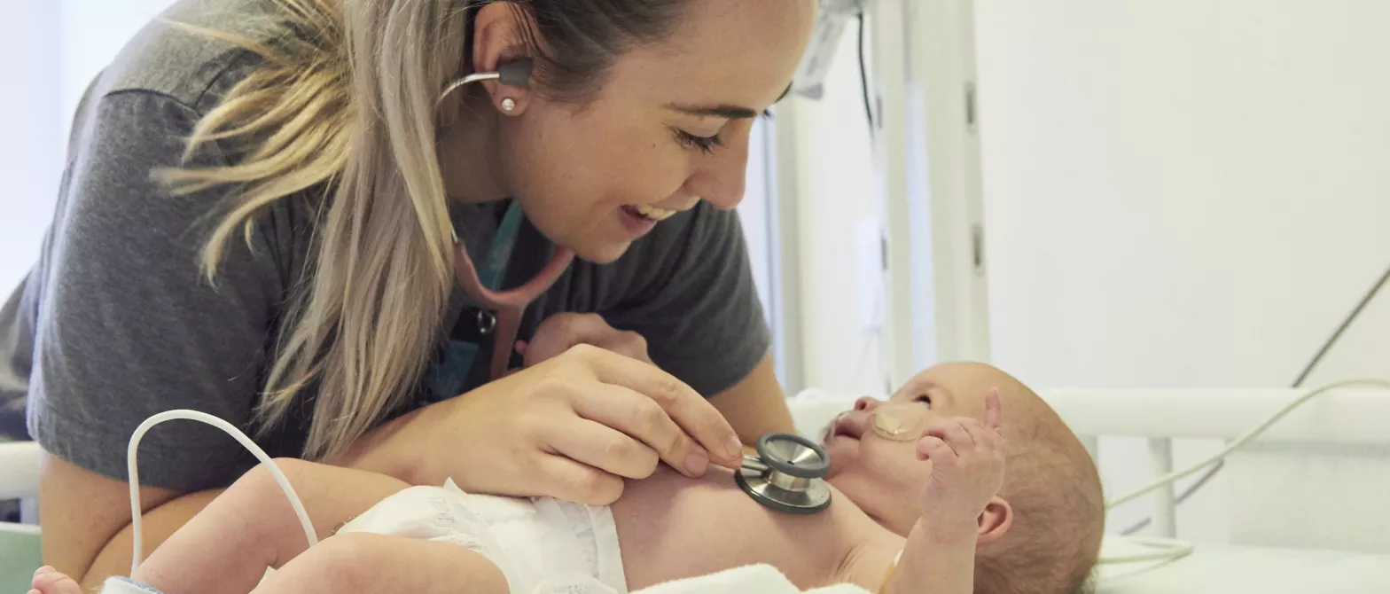 A nurse checks the heartbeat of a smiling baby