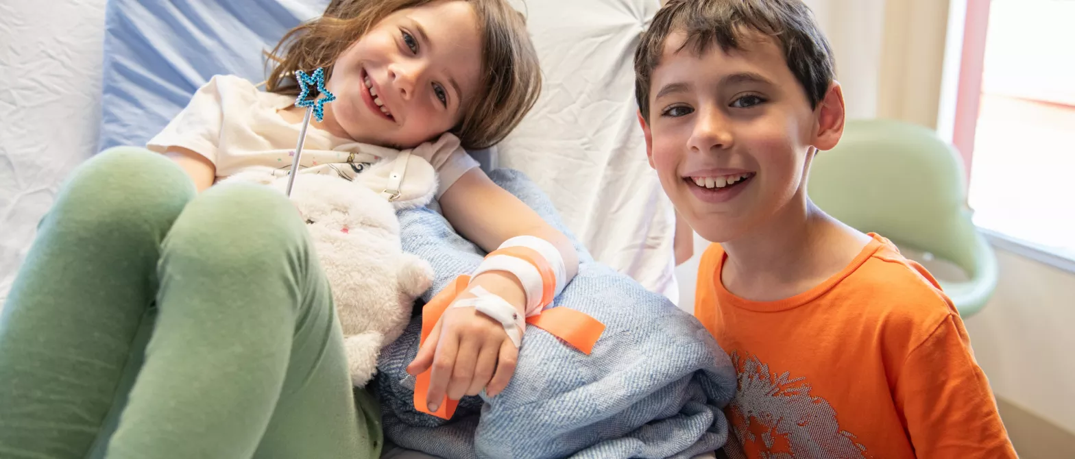 A child smiling while visiting their sibling in a hospital bed. 