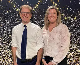 Sarah Walker and Adrian Dix pose in front of a sparkled background