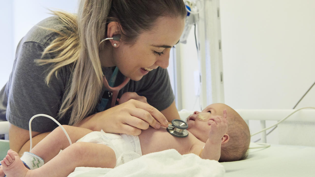 A nurse checks the heartbeat of a smiling baby