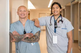 Two nurses pose for a photo in a hospital hallway