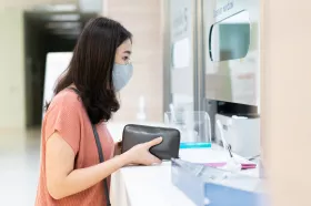 Woman in mask holding wallet by cashier window