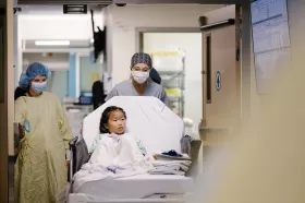Child in gown being wheeled on bed by two surgical team members