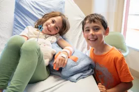 A child smiling while visiting their sibling in a hospital bed. 