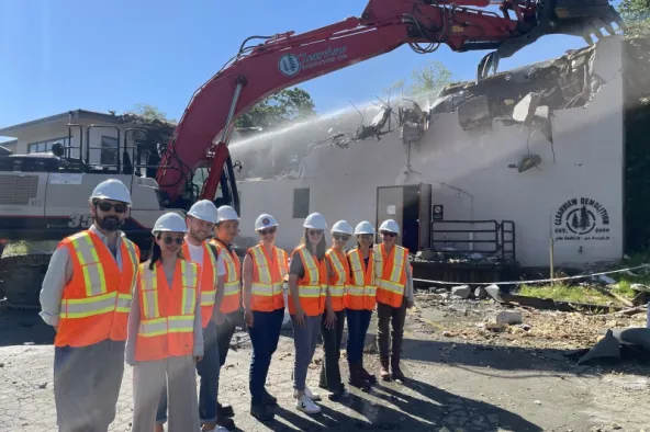 Slocan Site Redevelopment Project team posing in front of an excavator beginning the demolition