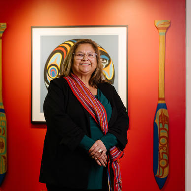 An Indigenous woman poses for a photo in front of traditional Indigenous art